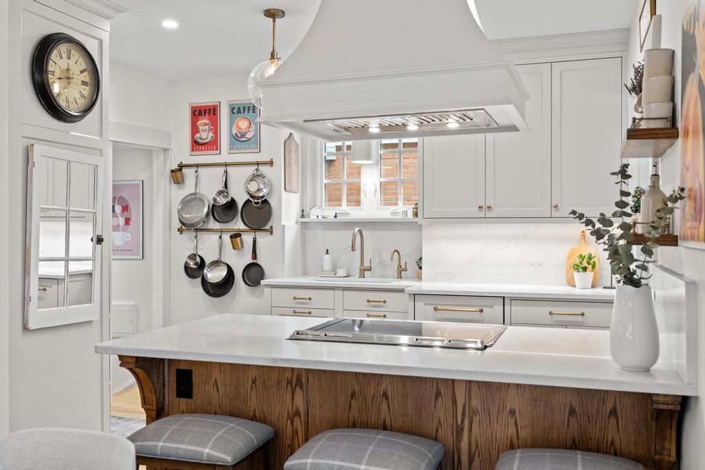 Bright modern kitchen with white cabinets, wood island, hanging pots, and stainless range hood