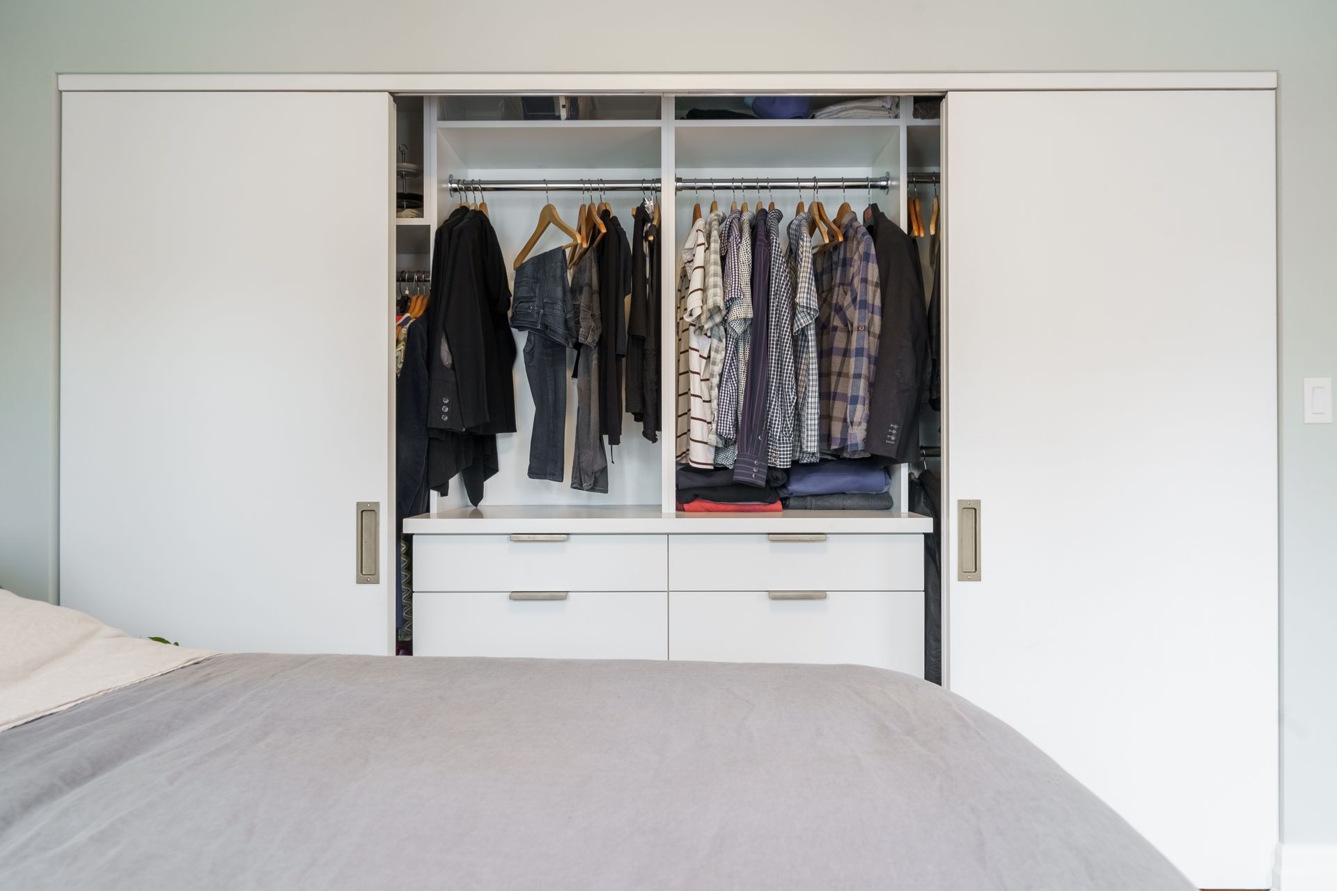 Open bedroom closet with hanging clothes and drawers, flanked by white sliding doors.