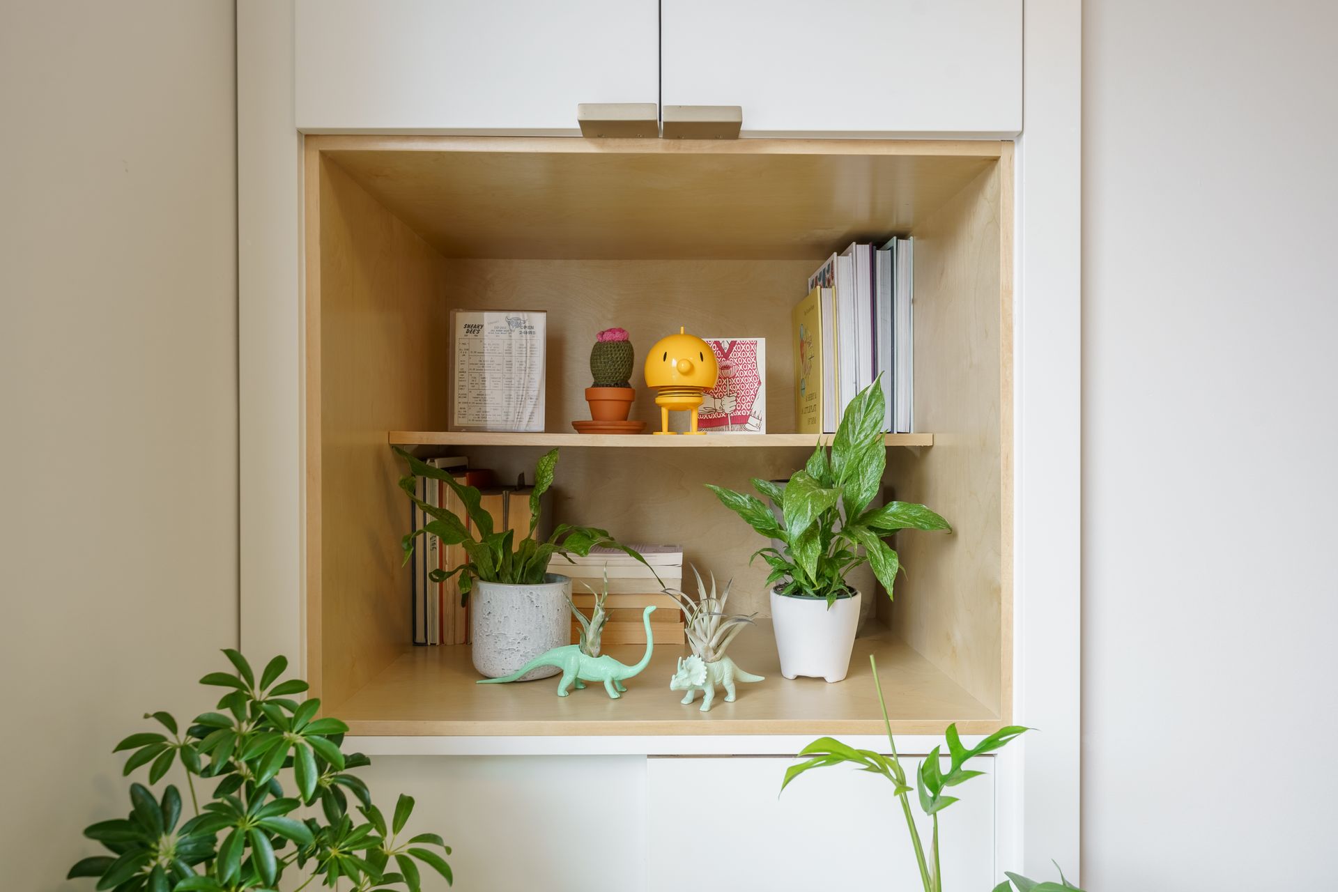 Wooden wall shelf with potted plants, books, and small decorative figurines