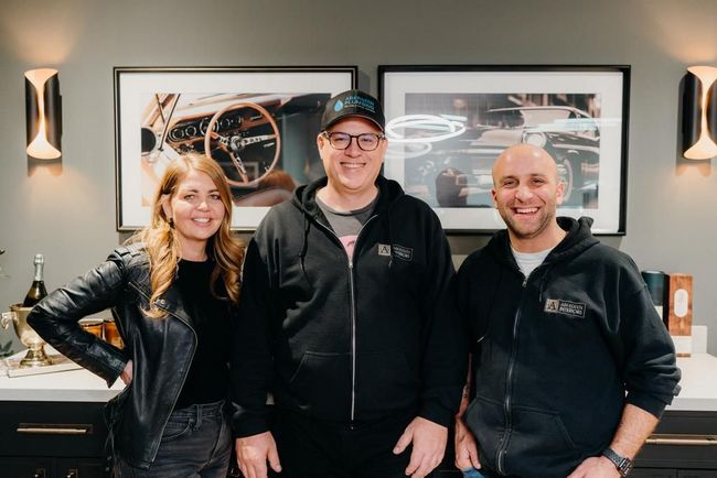 Three people smiling in black jackets in front of framed wall art