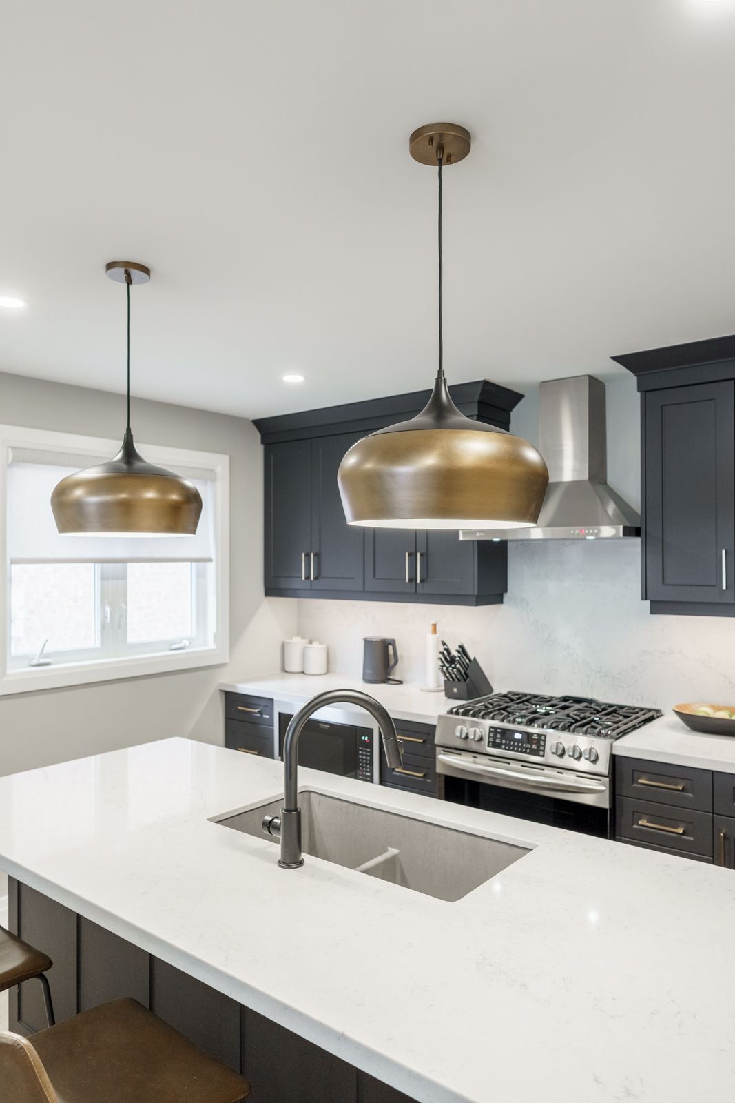 Modern kitchen with white island, gold pendant lights, dark cabinets, and stainless steel appliances
