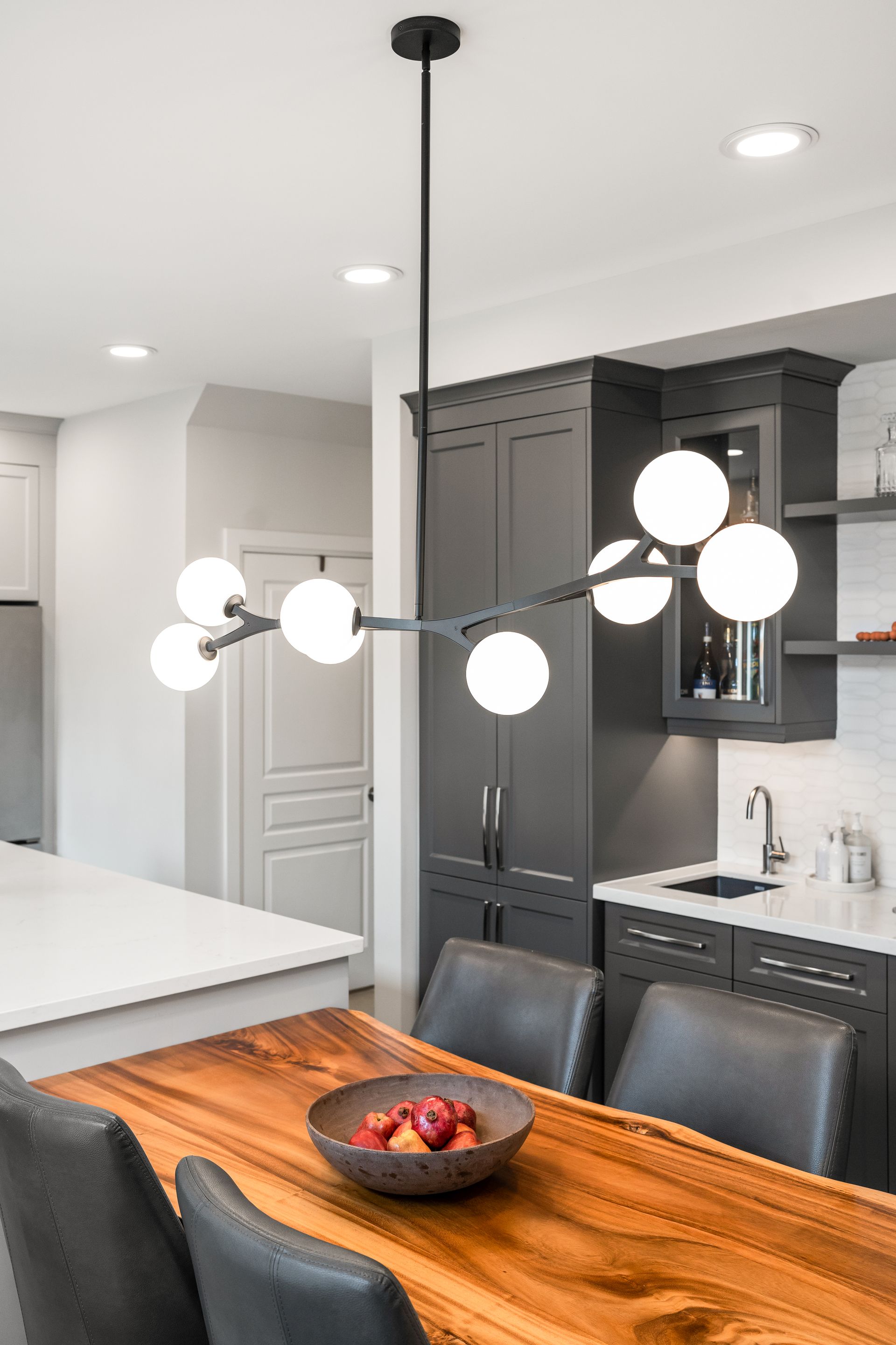 Modern kitchen with black cabinetry, white globe pendant lights, and a wooden dining table.