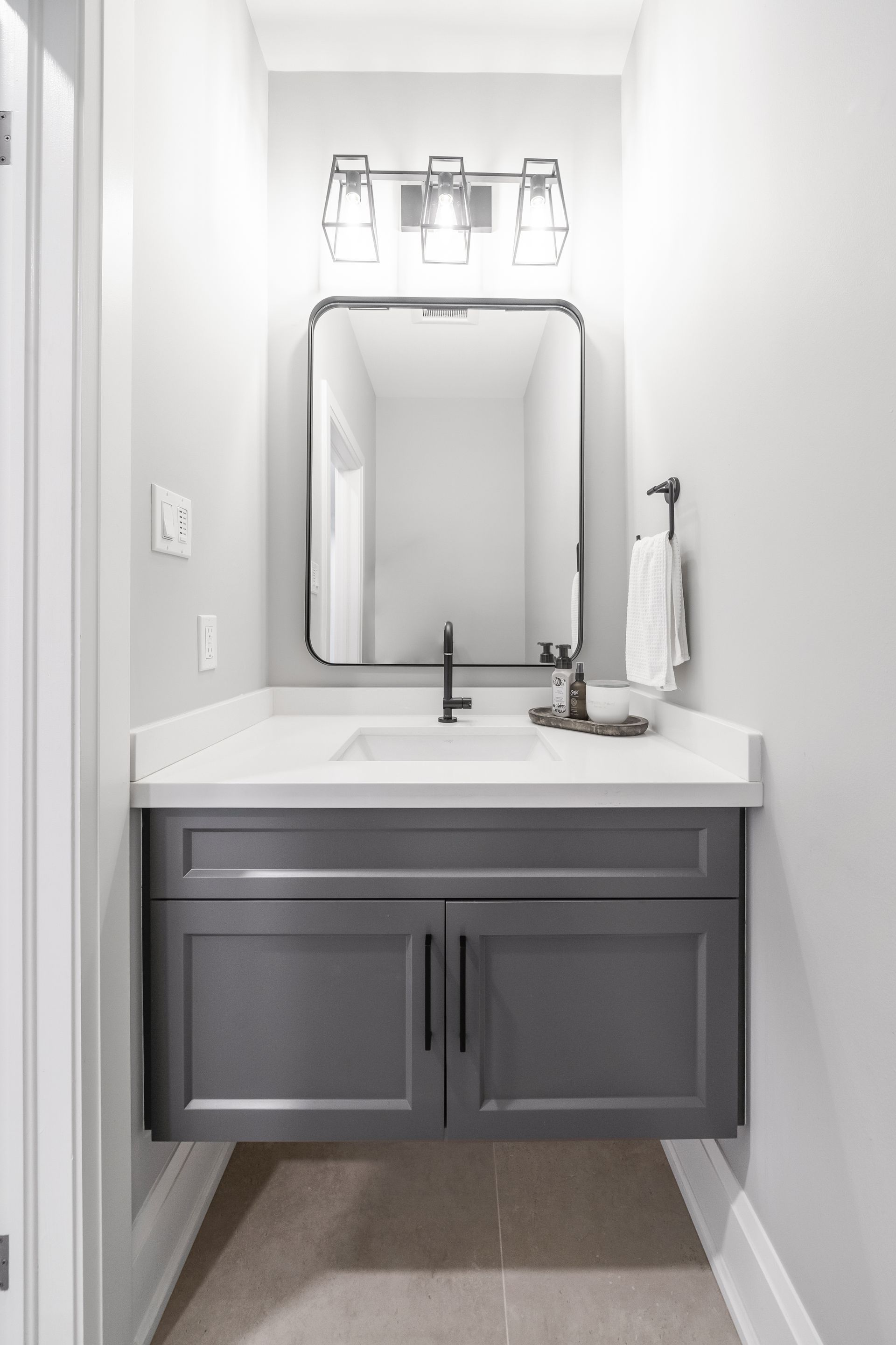 Small bathroom vanity with gray cabinet, white countertop, sink, mirror, and wall light.