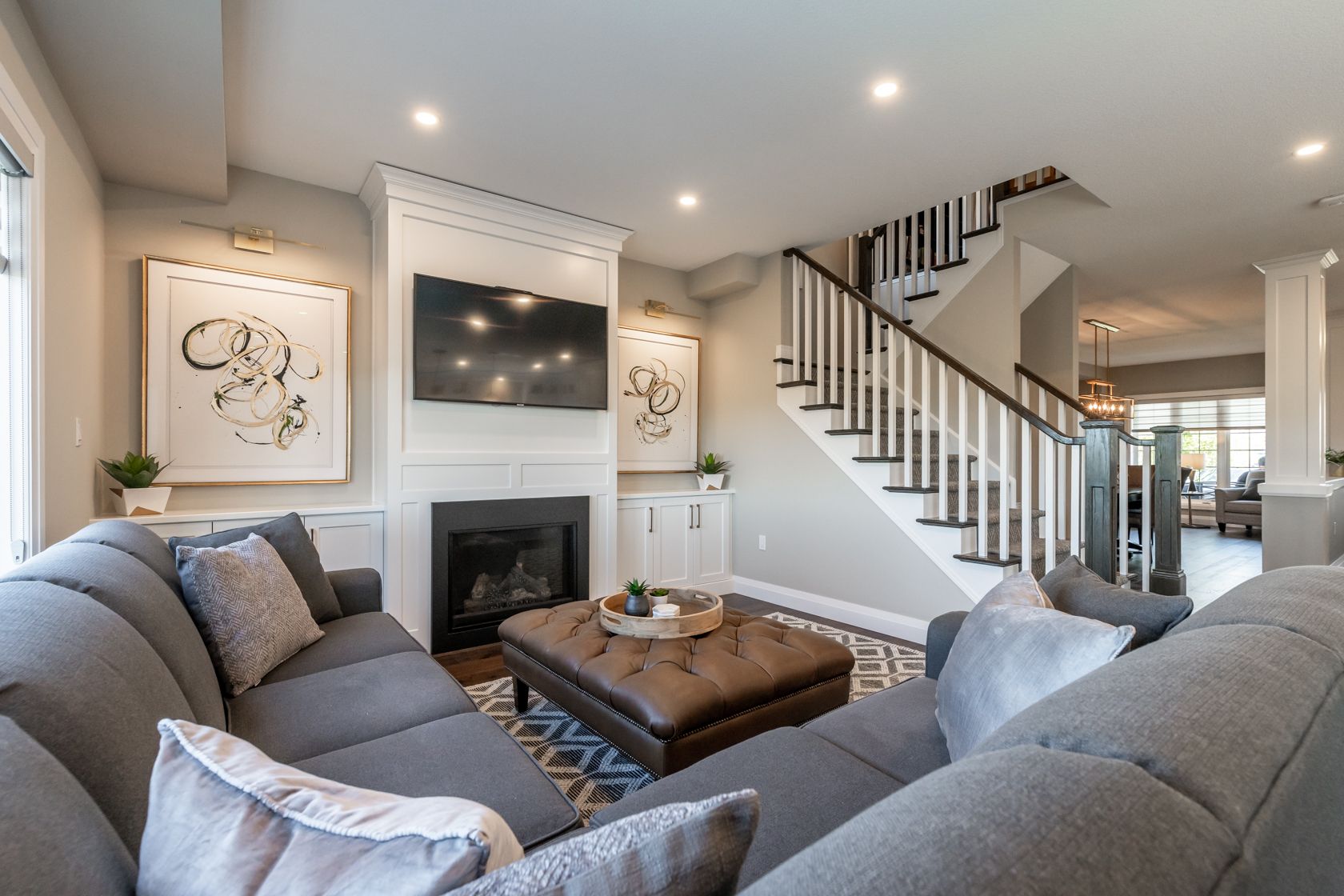 Bright living room with gray sofas, fireplace, wall art, and staircase leading upstairs