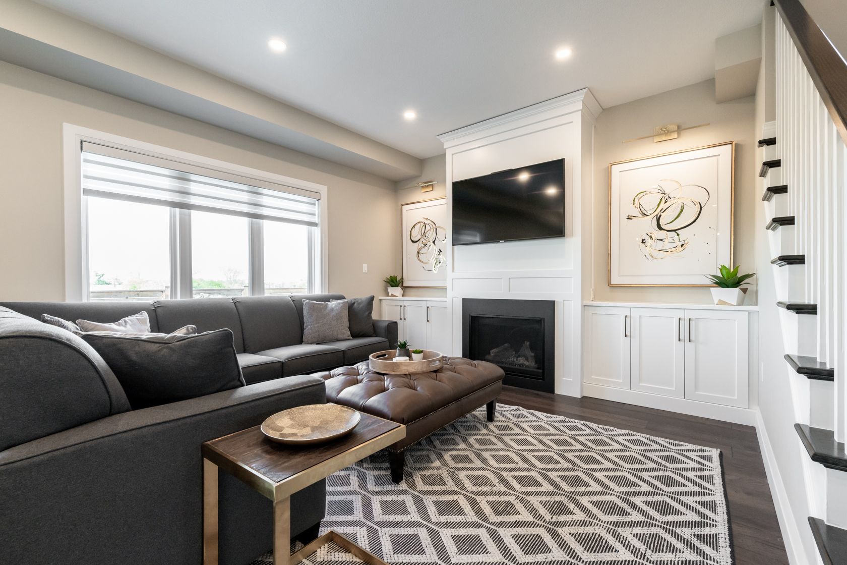 Bright living room with gray sectional, fireplace, wall-mounted TV, and patterned rug.