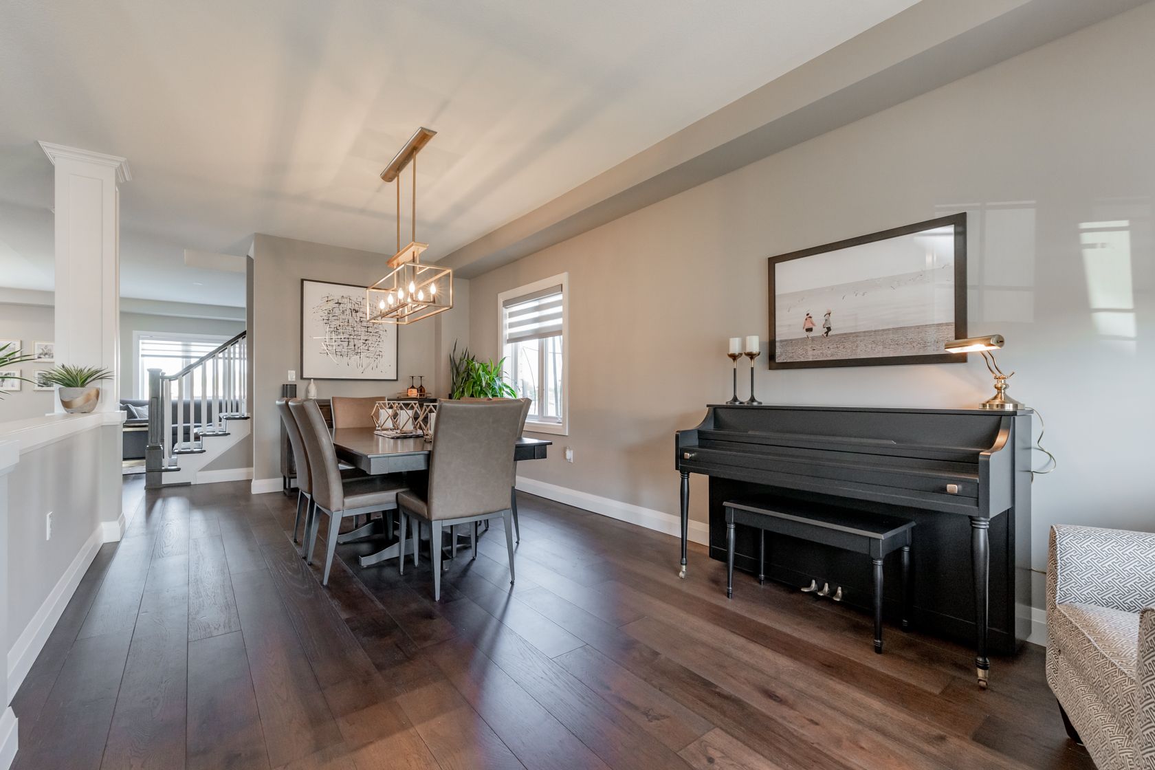 Open dining room with dark wood floors, chandelier, and black piano beside a bright wall mirror