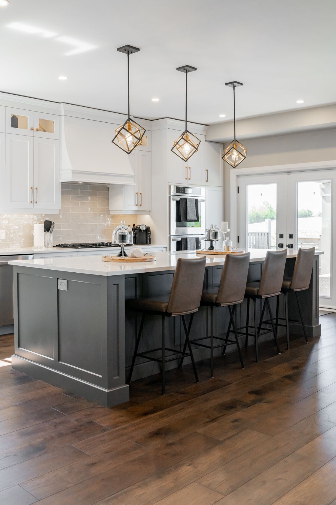 Modern kitchen with white cabinets, dark island, pendant lights, and barstools on hardwood floors