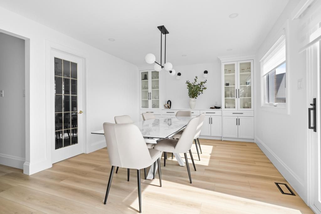 Bright dining room with white chairs, glass cabinets, wood floor, and large windows letting in sunlight