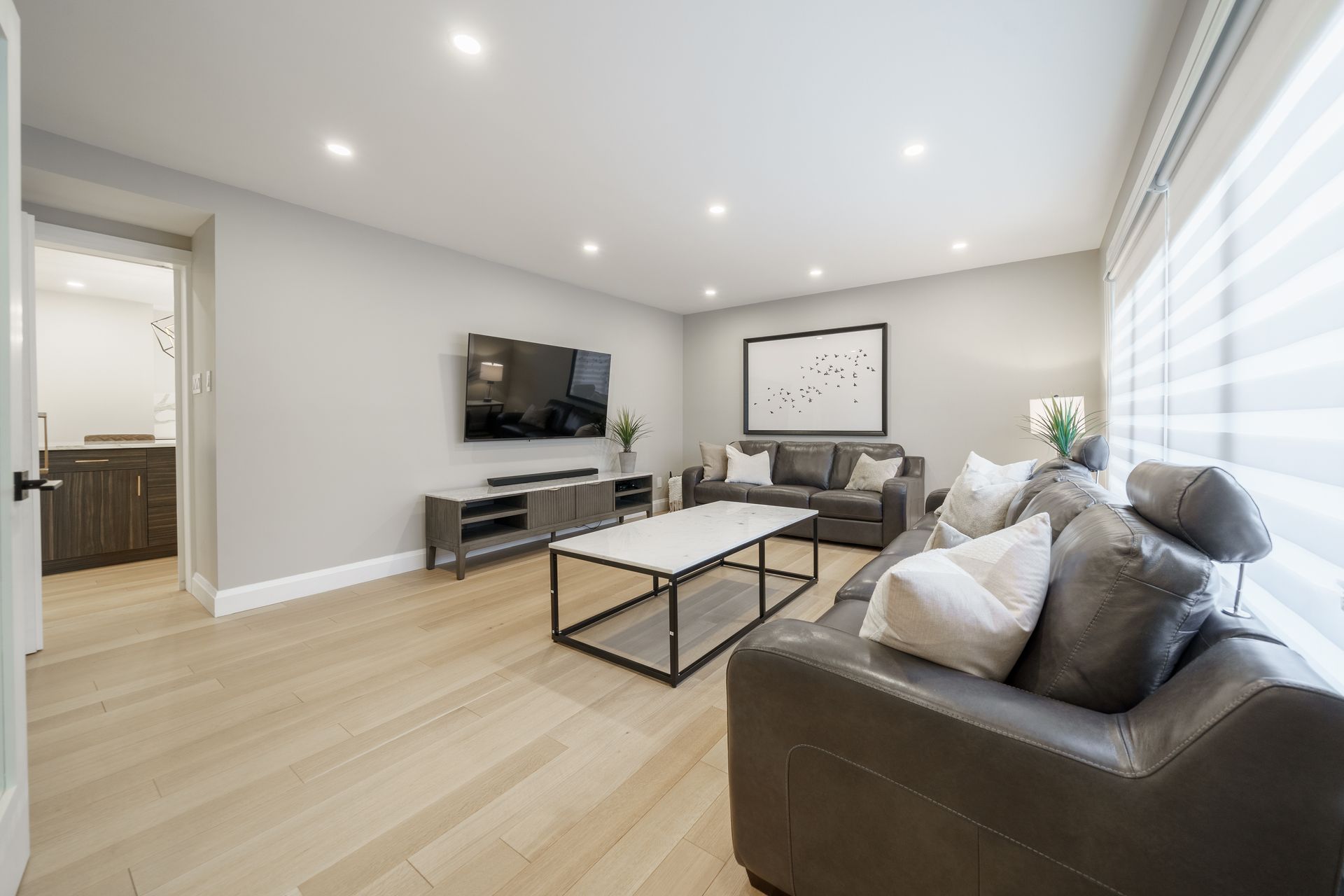 Bright modern living room with gray sofa, coffee table, wall TV, and large window blinds
