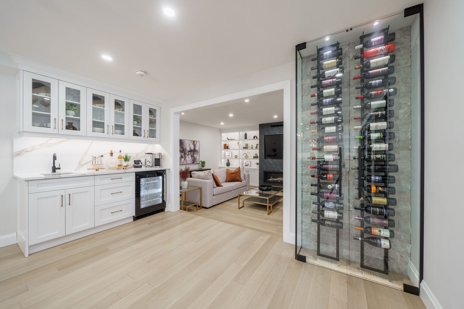 Bright modern kitchen with white cabinets, light wood floors, and a glass wine rack display.