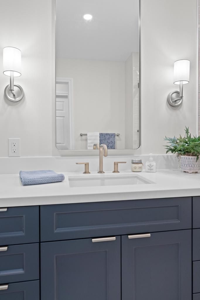 Modern bathroom vanity with dark blue cabinets, white countertop, mirror, sconces, and folded towels