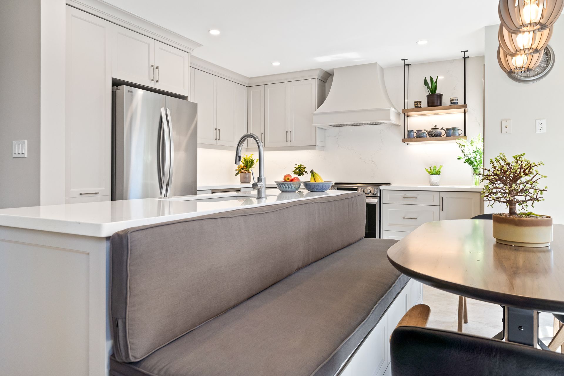 Bright modern kitchen with stainless steel appliances, white cabinets, and a gray upholstered bench by a round table
