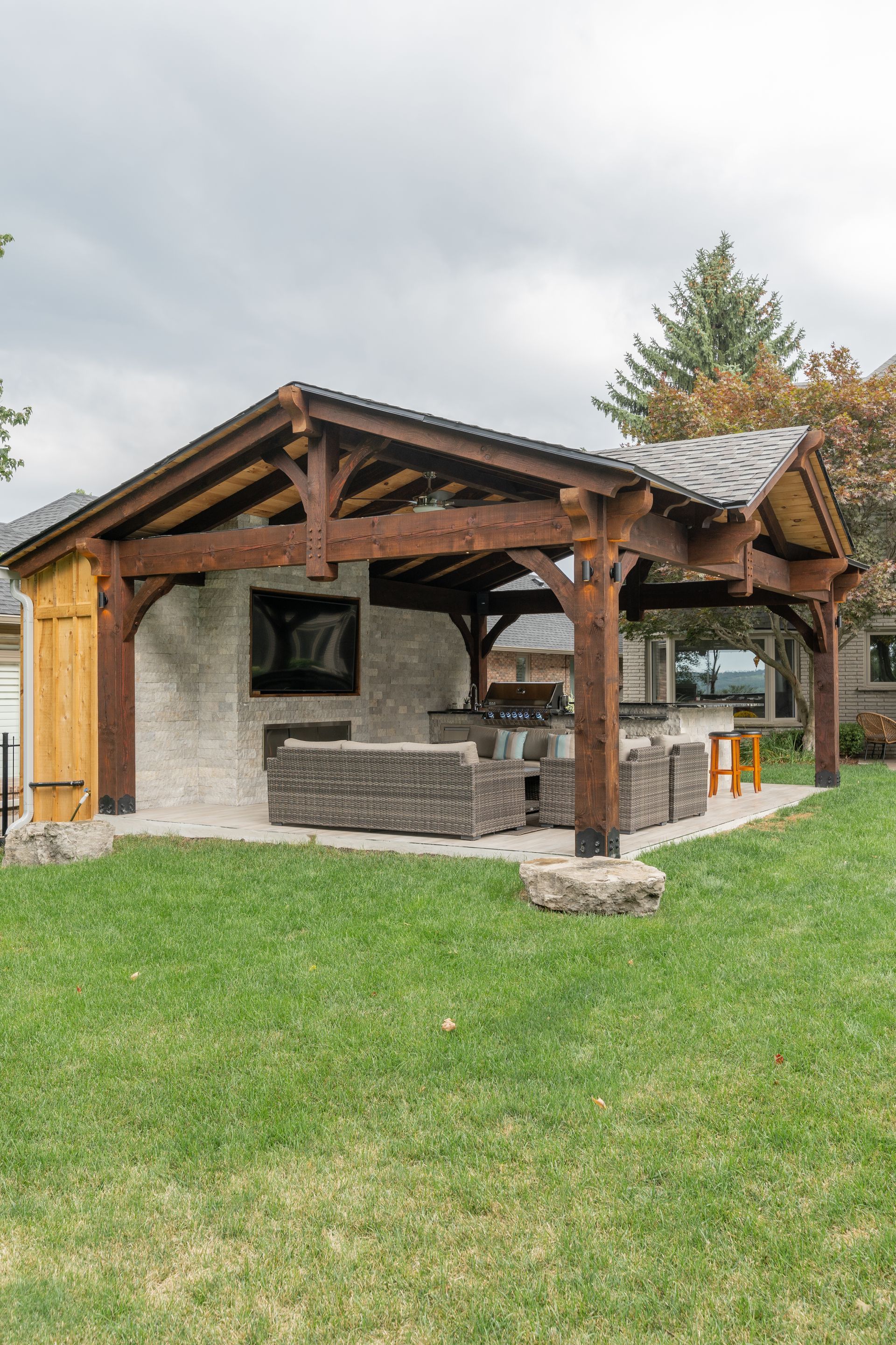 Stone outdoor pavilion with wooden roof and grassy lawn under a cloudy sky