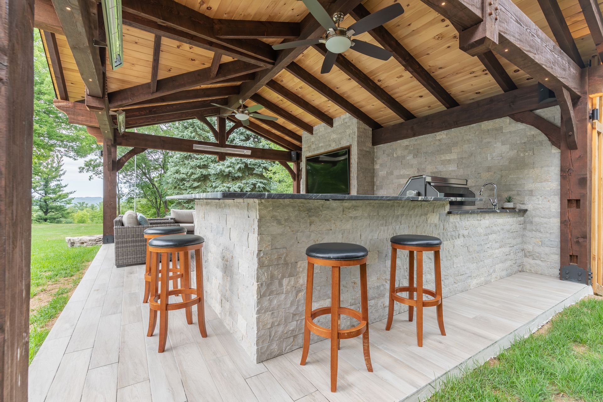 Outdoor covered patio with stone bar, wooden stools, and exposed timber beams
