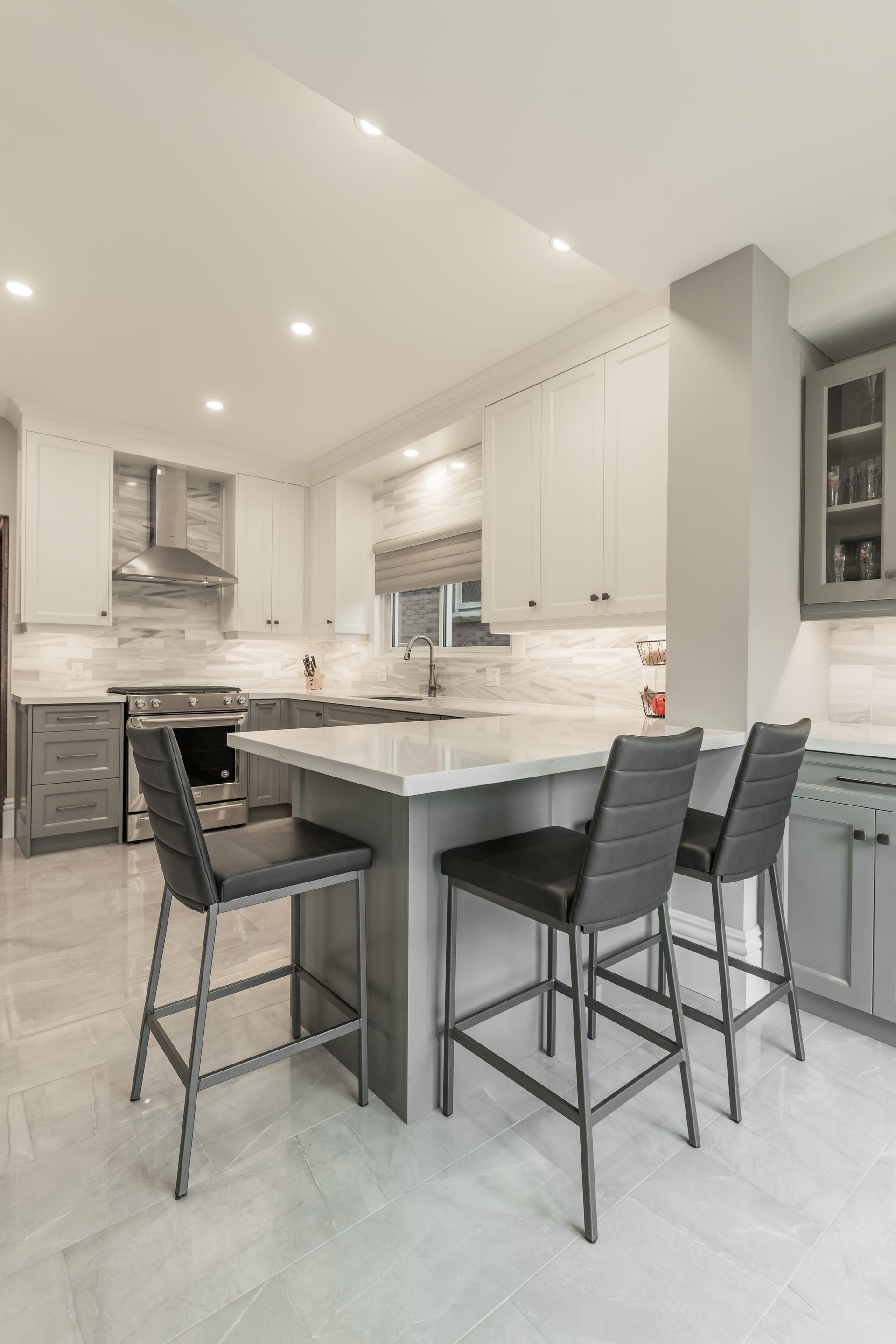 Modern kitchen with marble island, white cabinets, and three black barstools