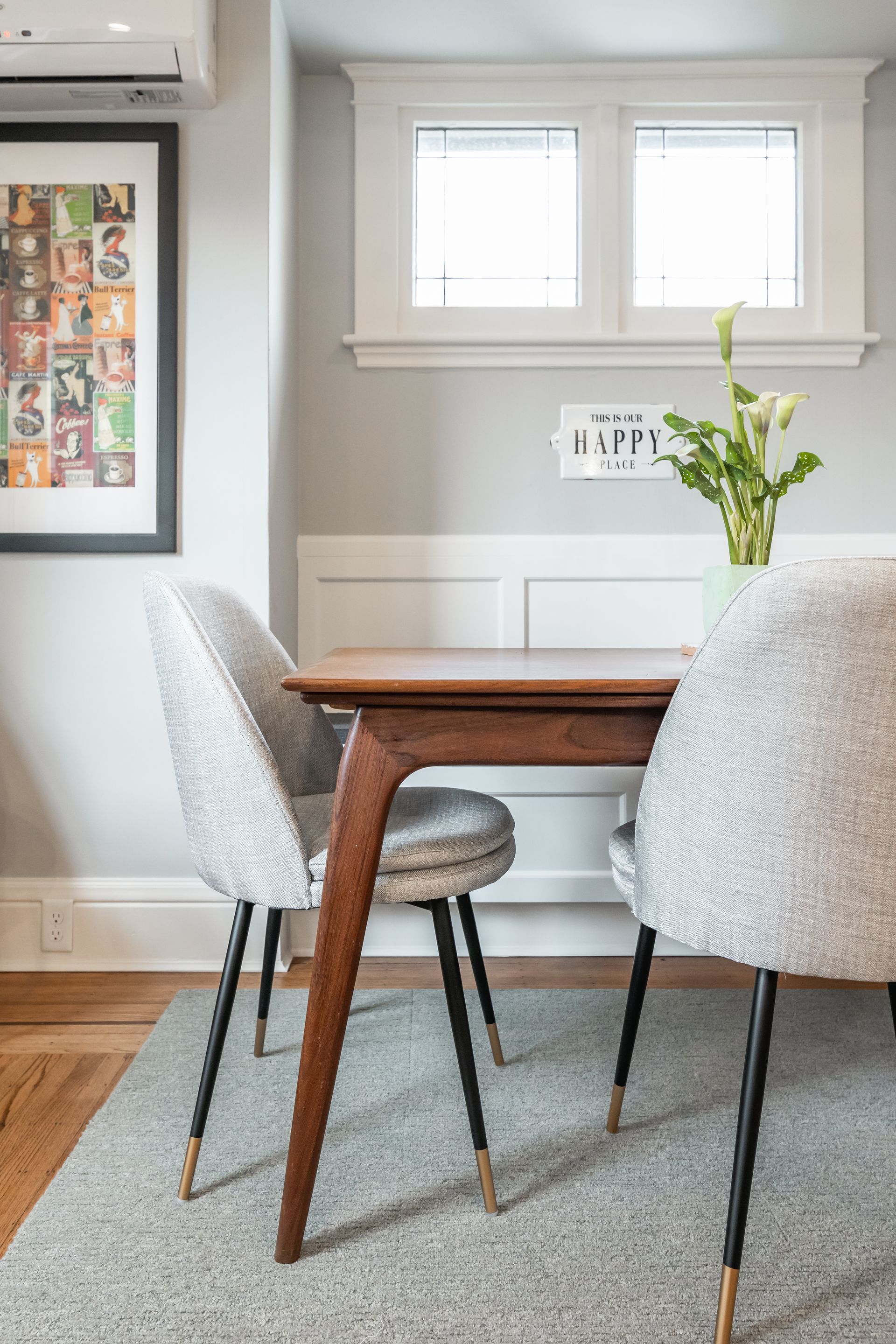 Dining nook with wooden table, textured gray chairs, and a vase of yellow flowers beneath a window