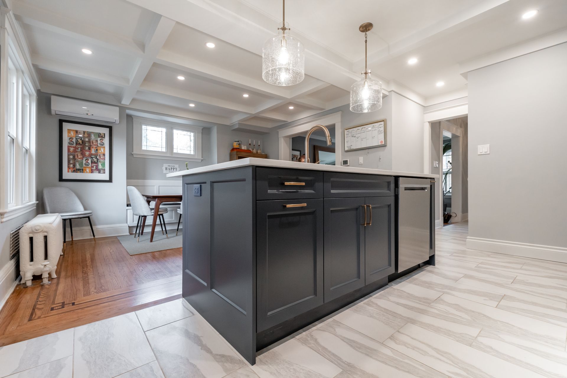 Modern kitchen with dark island, white cabinets, and open dining area with hardwood floors
