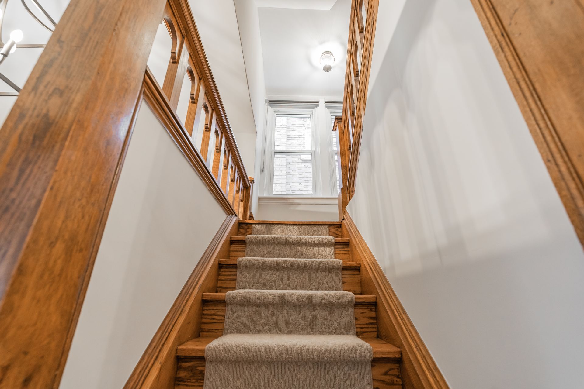 Carpeted wooden staircase in a bright hallway with white walls and a door at the top.