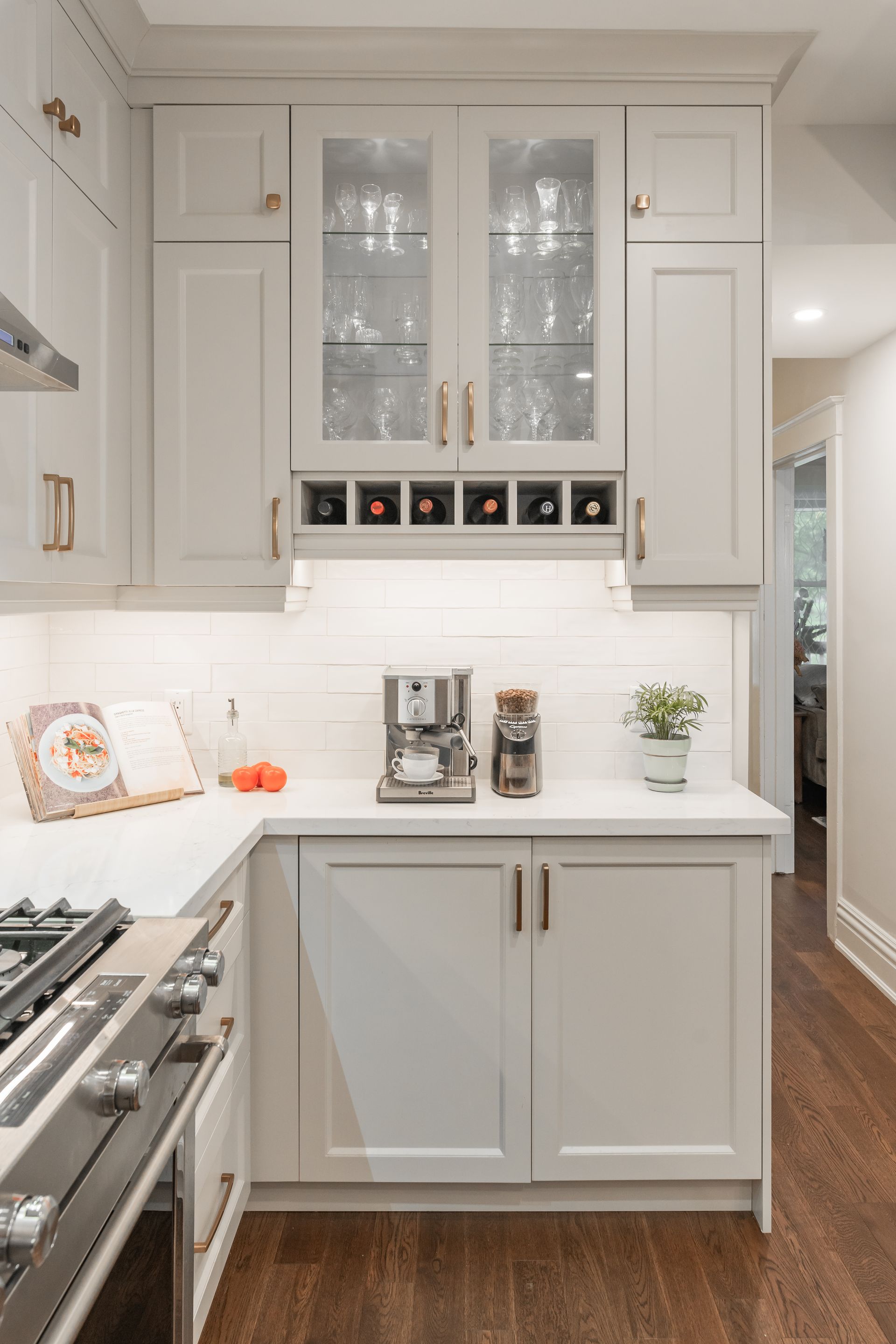 Bright white kitchen with glass-front cabinets, stainless stove, and coffee maker on the counter
