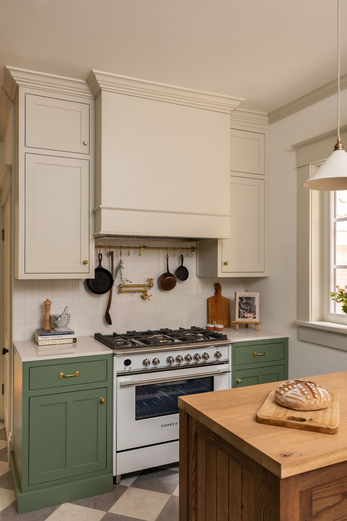 Bright kitchen with green cabinets, white stove, hanging utensils, and a wooden island with bread.