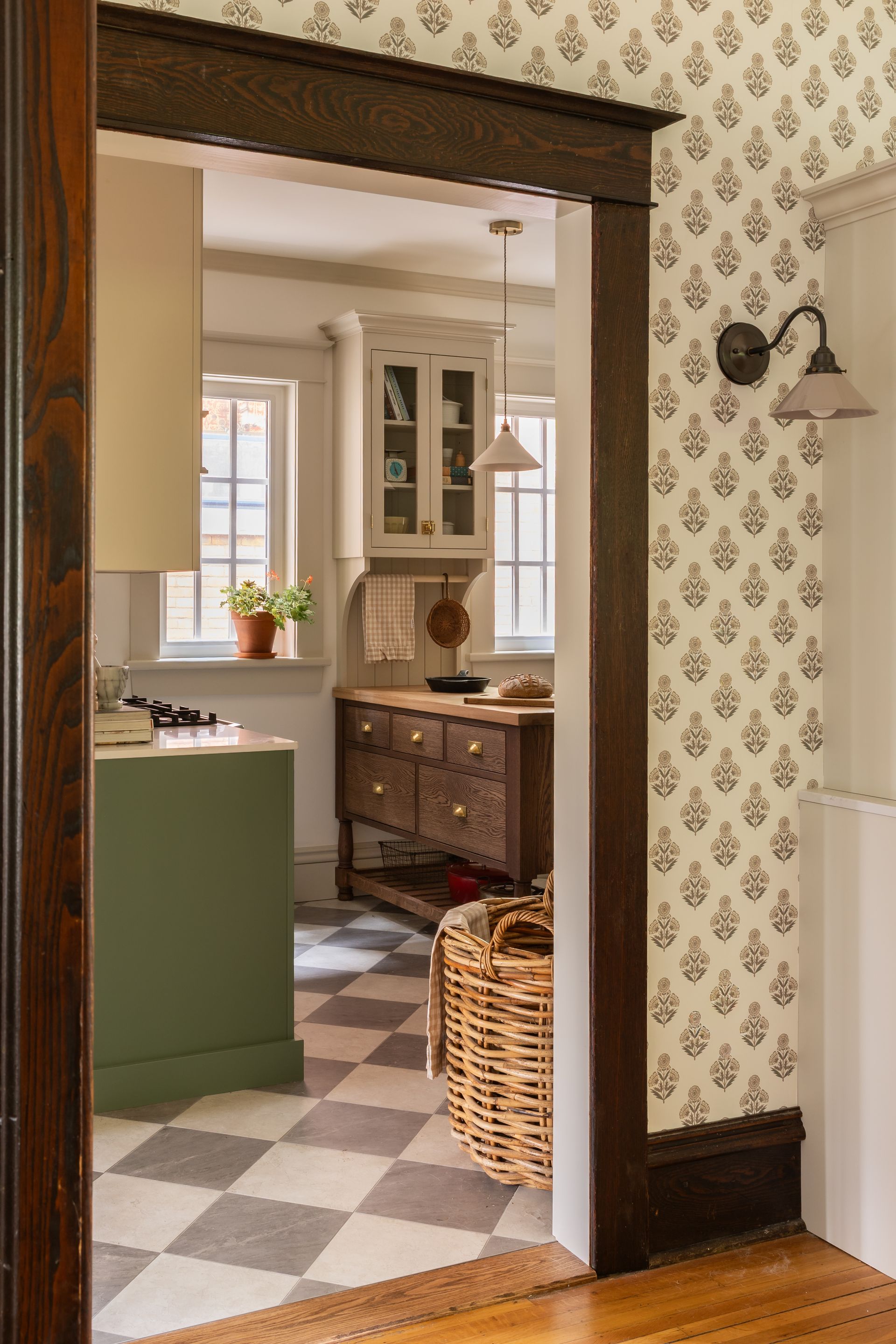 Dining room with wooden table, hutch, patterned wallpaper, and hanging pendant light.