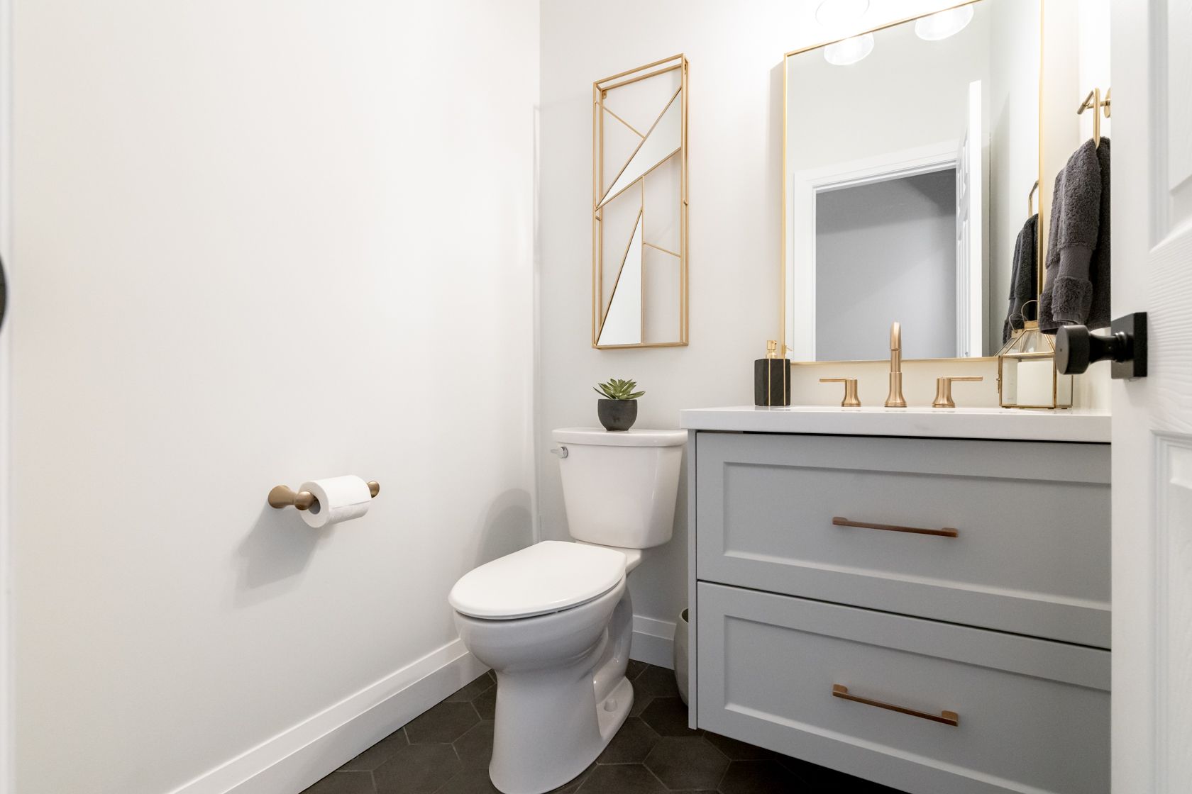Modern white bathroom with toilet, gray vanity, large mirror, and gold accents