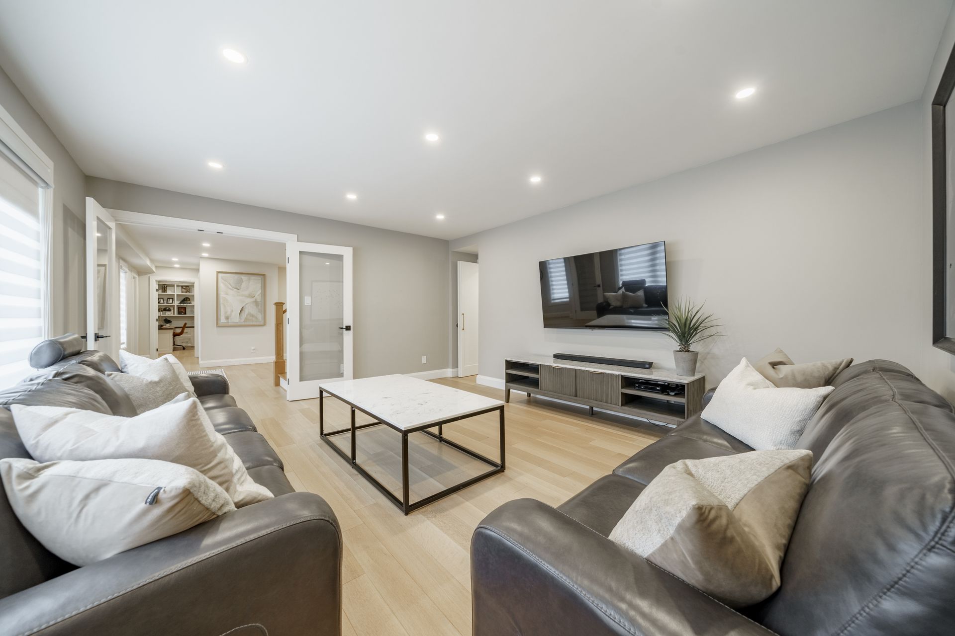 Modern living room with gray sofas, white coffee table, wall-mounted TV, and recessed ceiling lights