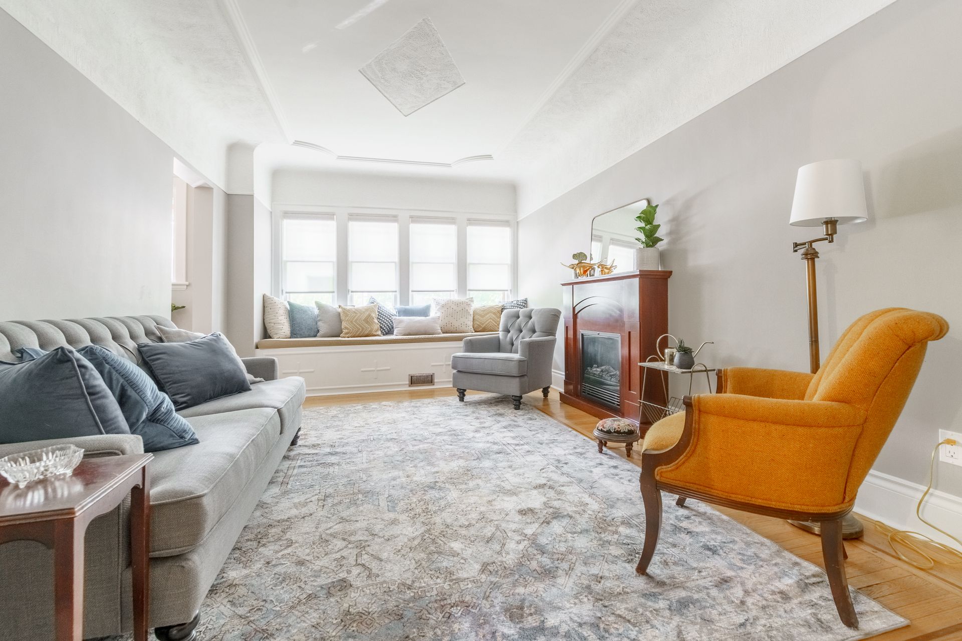 Bright living room with gray sofa, orange chair, fireplace, and sunlit window seat