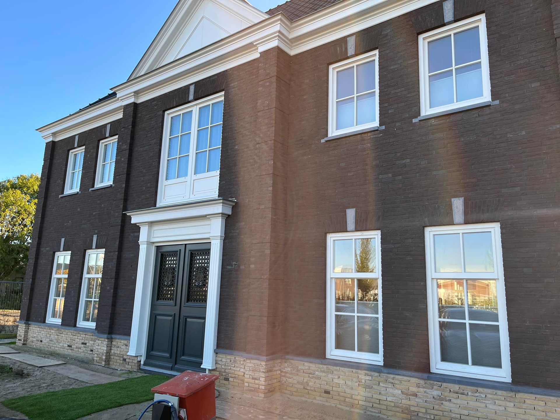 Donker bakstenen gebouw met witte raamkozijnen en een zwarte deur; exterieurfoto.