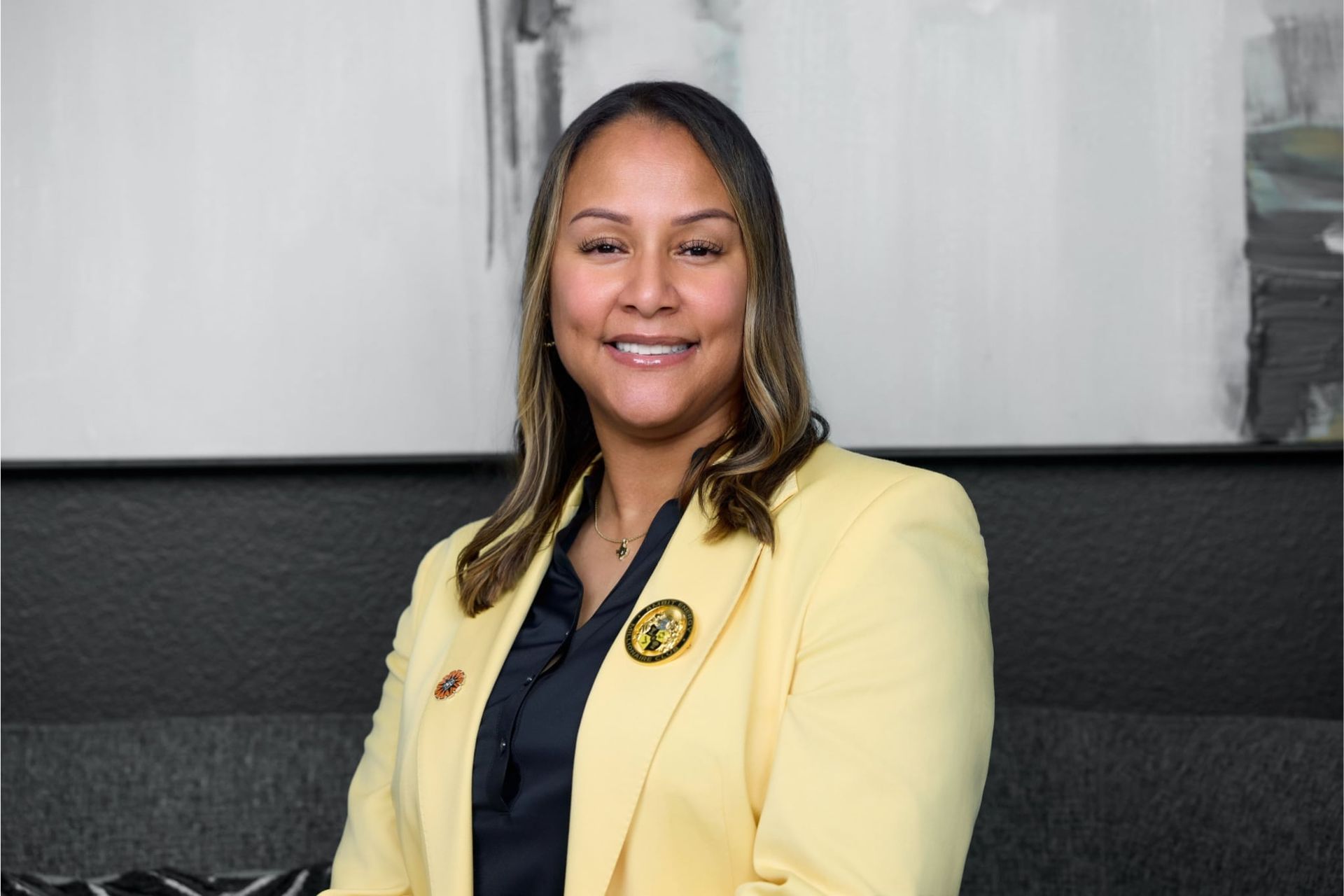 Alisha James, Smiling woman in a yellow blazer seated against a gray wall