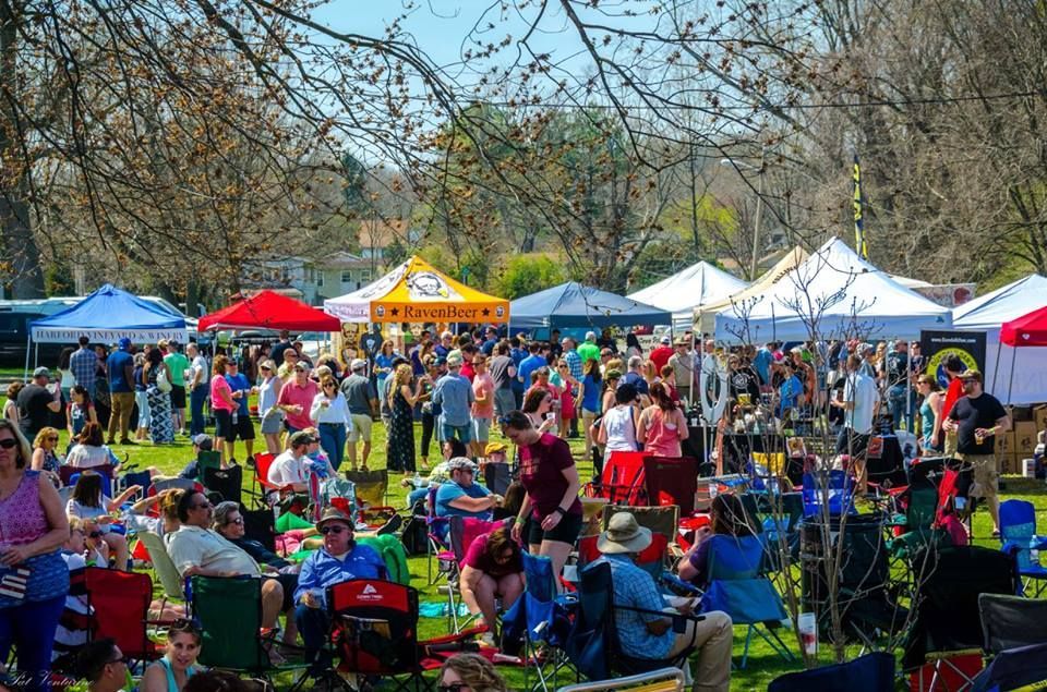 Crowd at outdoor festival on a sunny day, tents, people sitting in chairs.