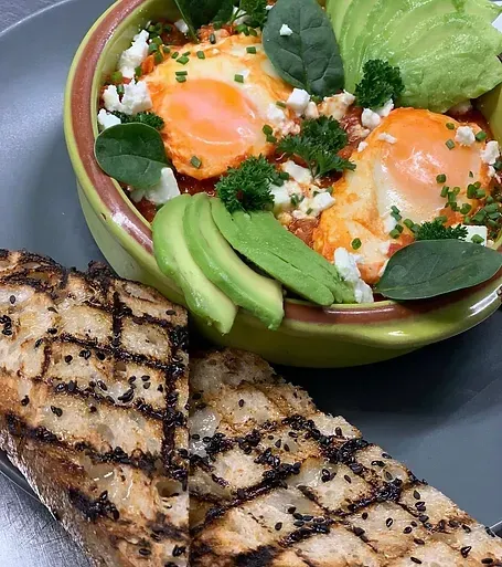 A bowl of food with eggs , avocado and toast on a plate.