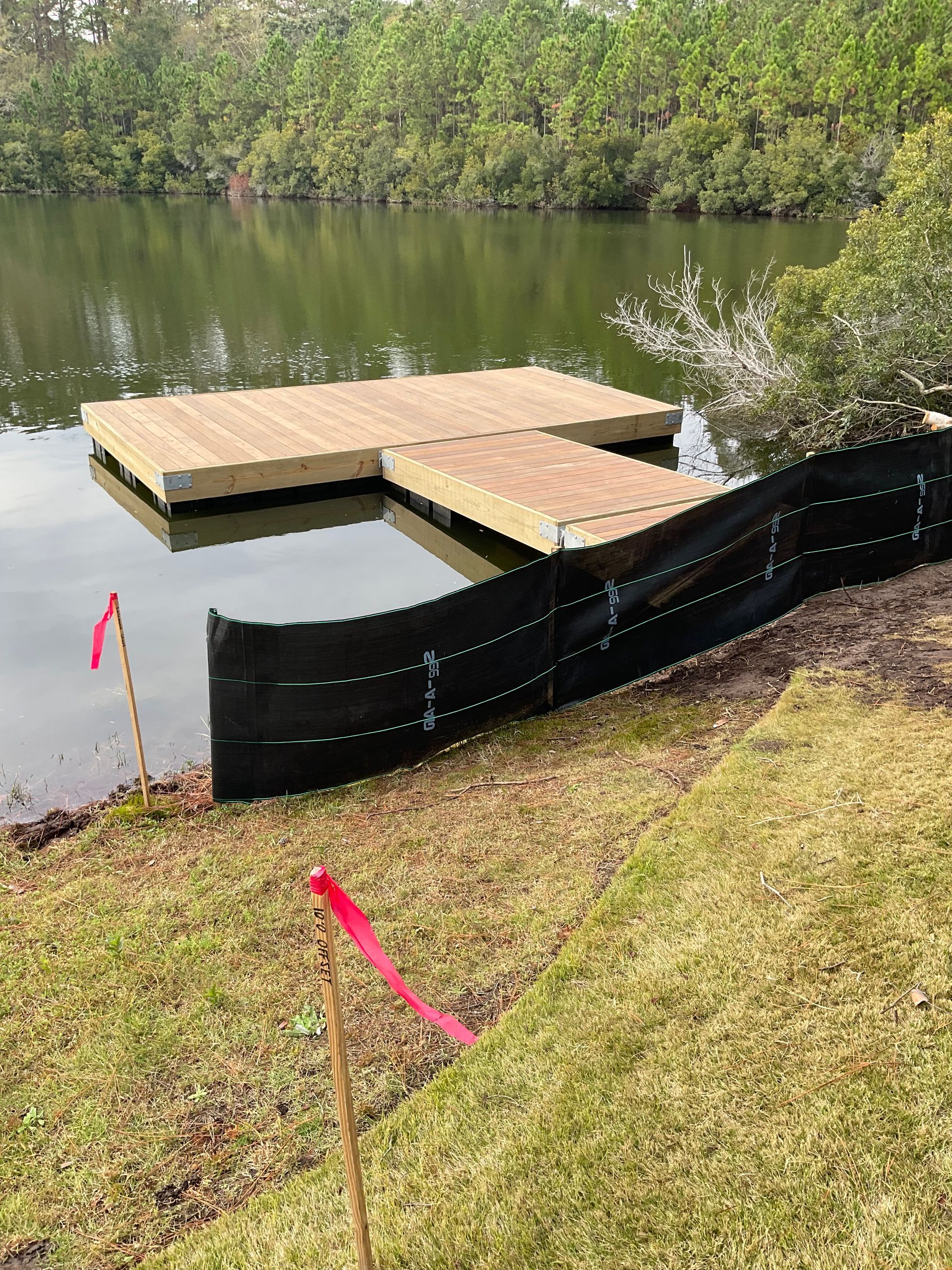 A dock is sitting on the shore of a lake next to a fence.