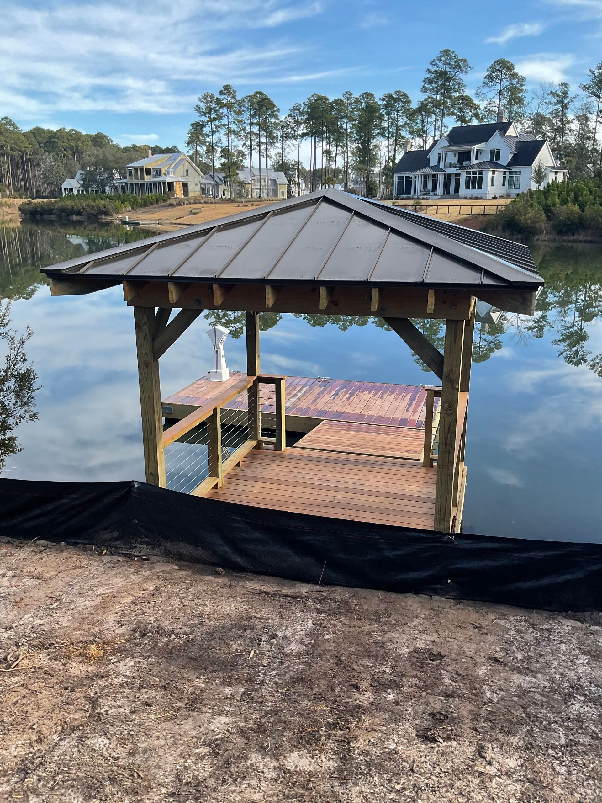 A wooden gazebo overlooking a lake with a house in the background.