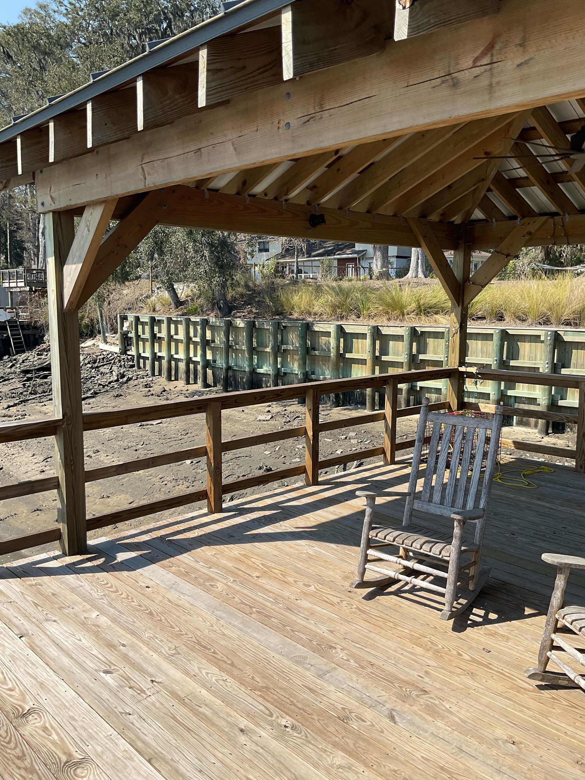 A wooden deck with a rocking chair under a wooden structure.