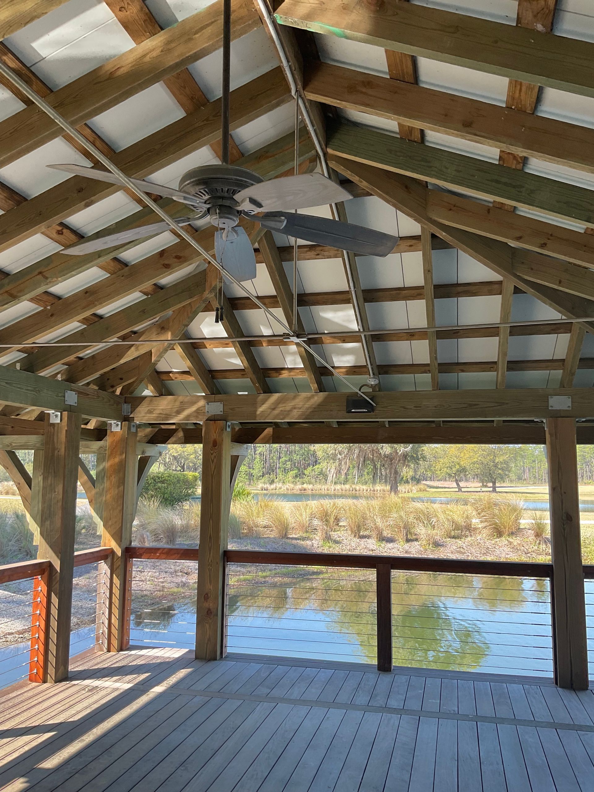 A ceiling fan is hanging from the ceiling of a wooden structure overlooking a body of water.