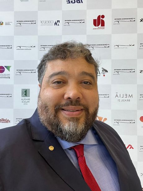 Um homem de terno e gravata está sorrindo em frente a uma parede com logotipos.