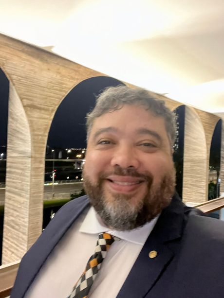 Um homem com barba está vestindo terno e gravata e sorrindo.