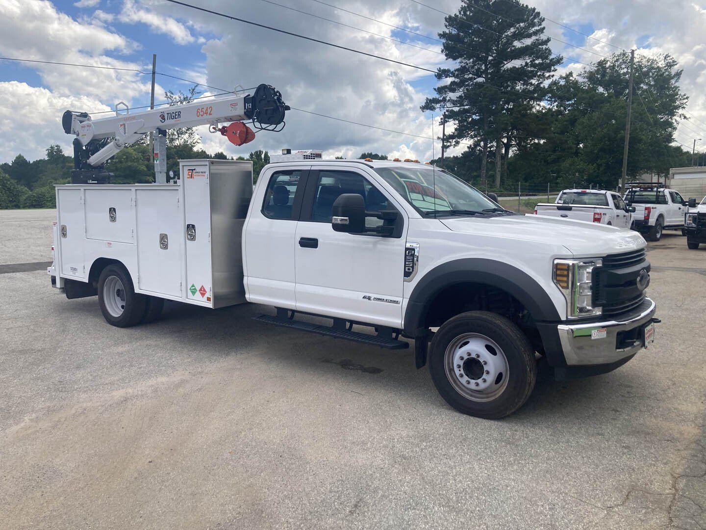 A white utility truck with a crane on top of it is parked in a parking lot.