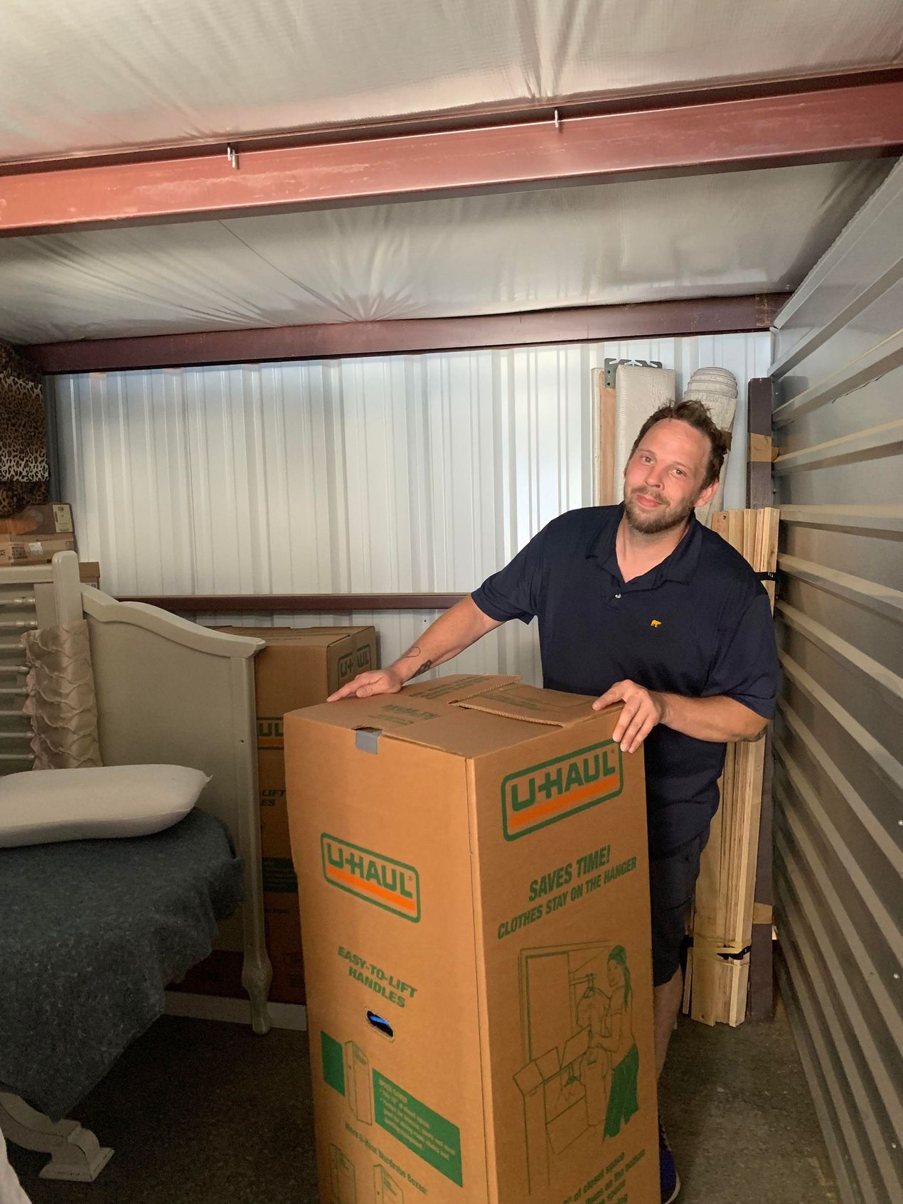A man is standing next to a large cardboard box in a storage unit.