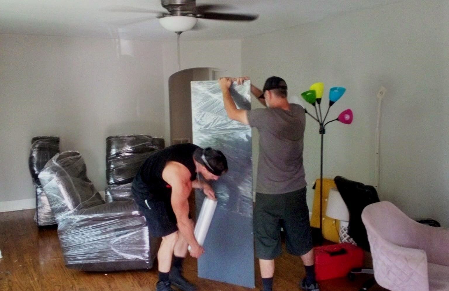 Two men are wrapping a piece of plastic in a living room