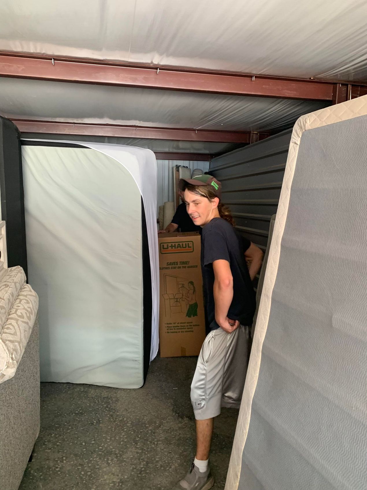 A boy is standing in a storage unit with a mattress and a box.