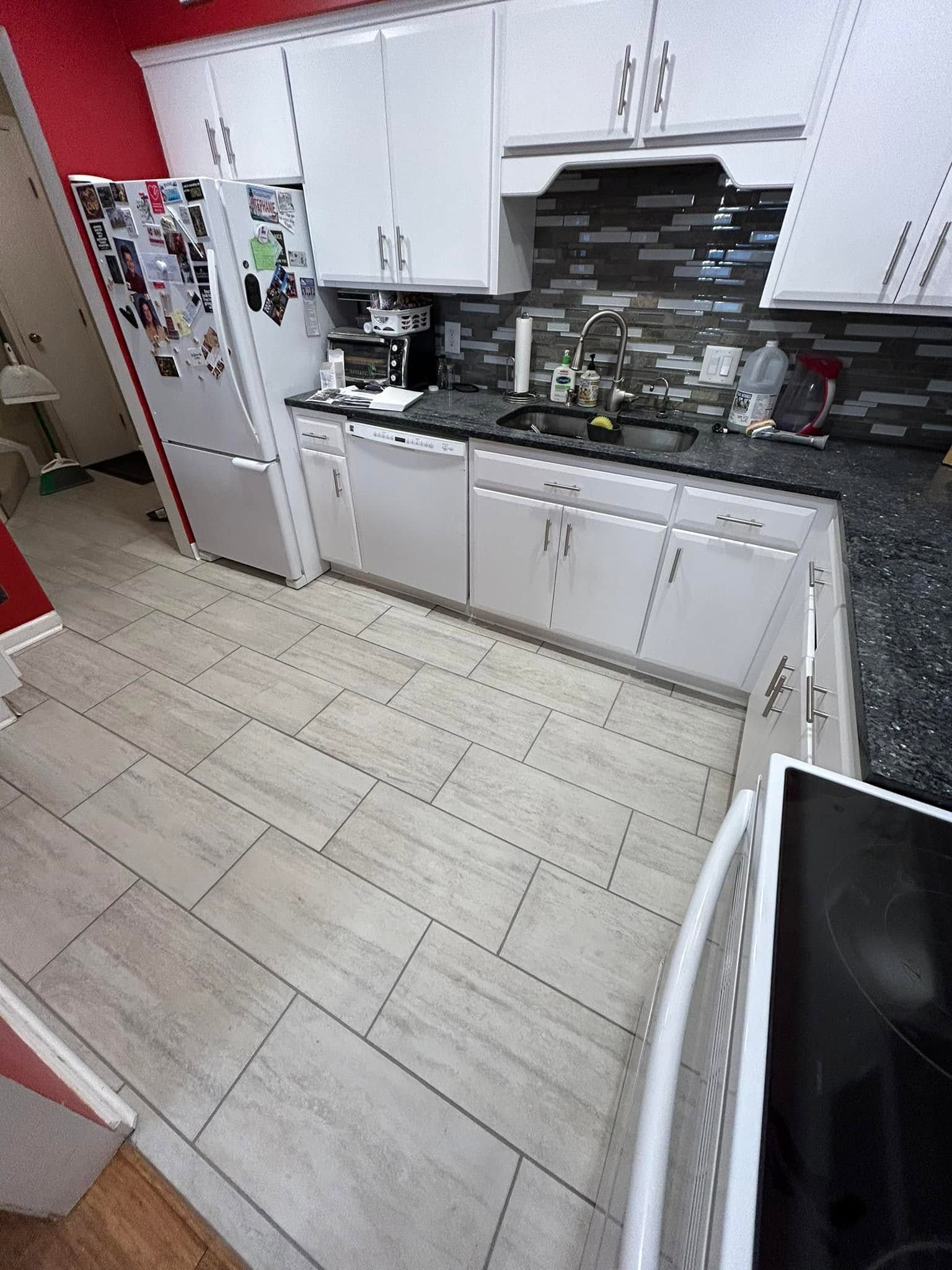 Modern kitchen with white cabinets, black countertop, tiled backsplash, and a refrigerator on the left