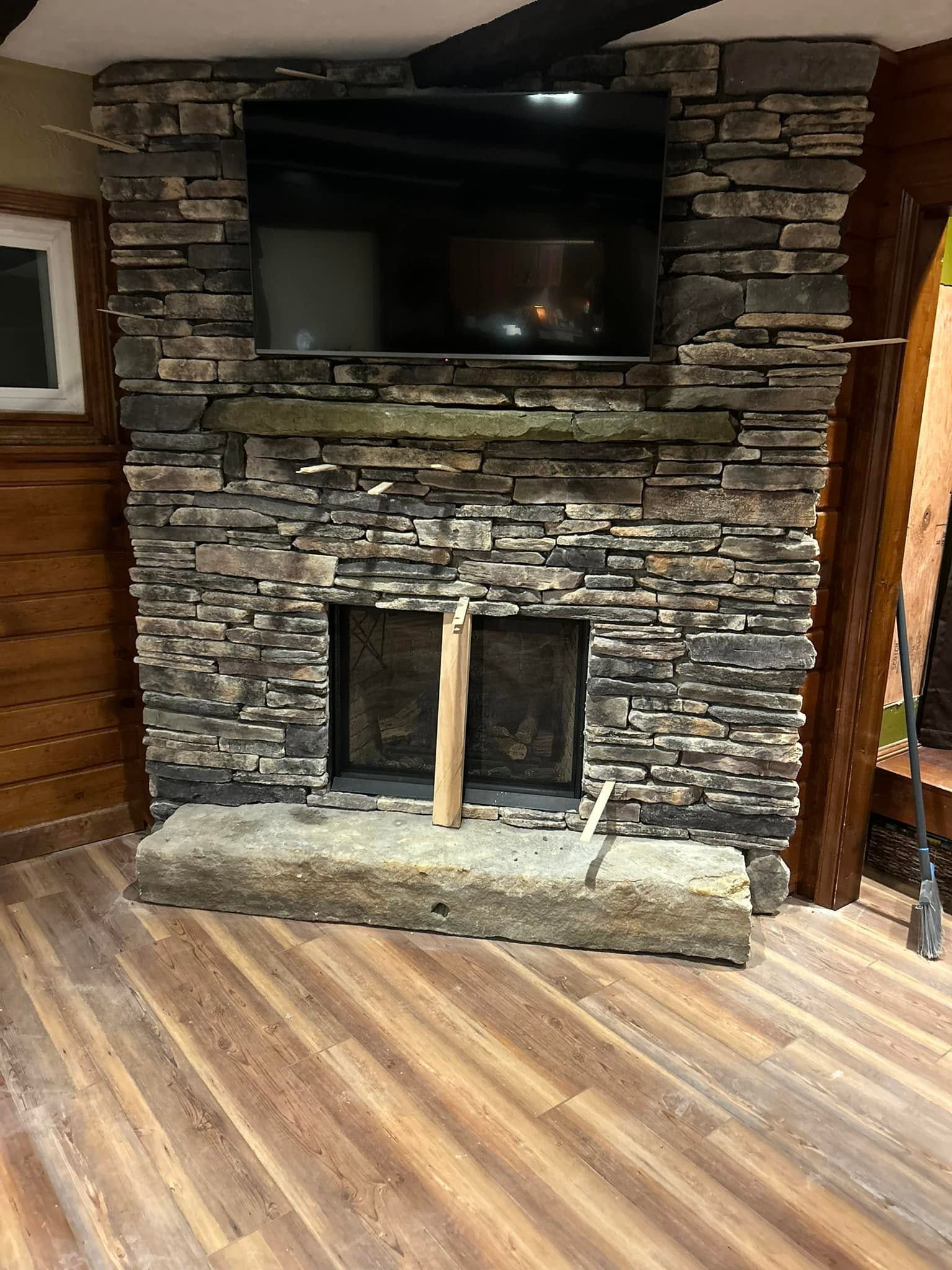Stone fireplace with a mounted TV above, set in a rustic room with wood flooring.