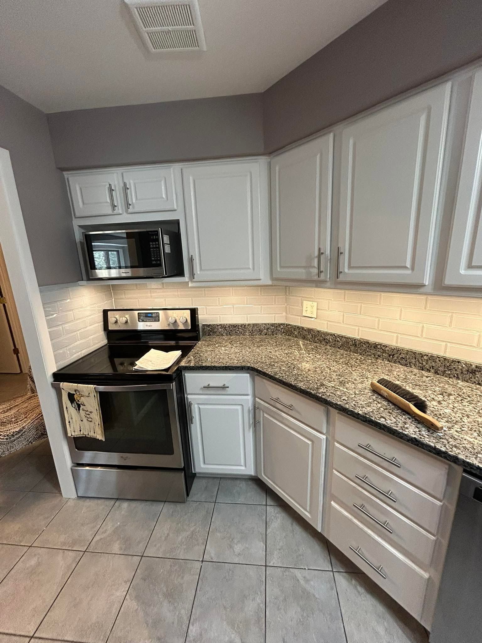 Modern kitchen with white cabinets, granite countertops, stainless steel appliances, and tile floor