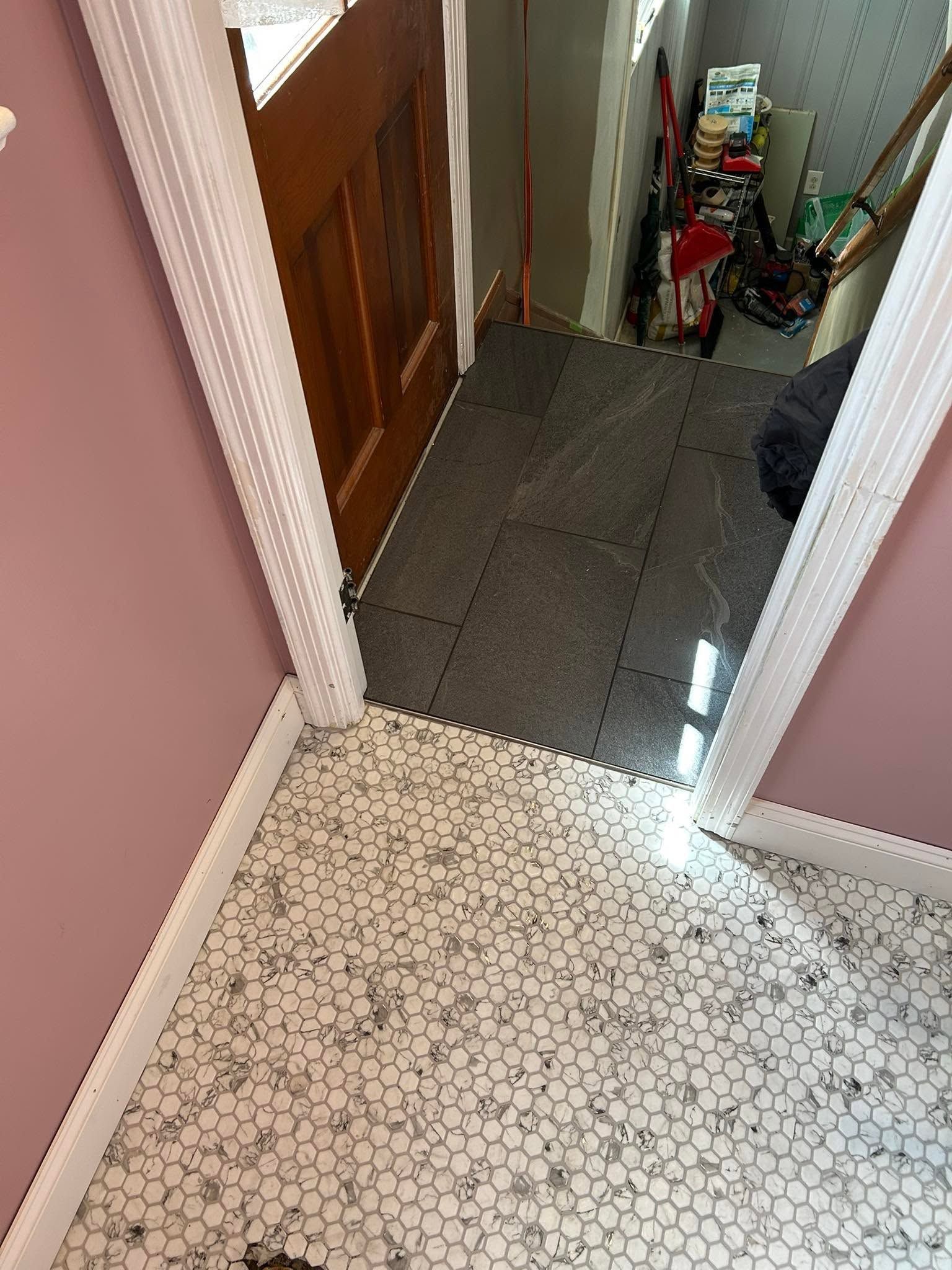 Hallway with patterned tile floor, wood door, and a narrow stairway landing with cleaning tools.
