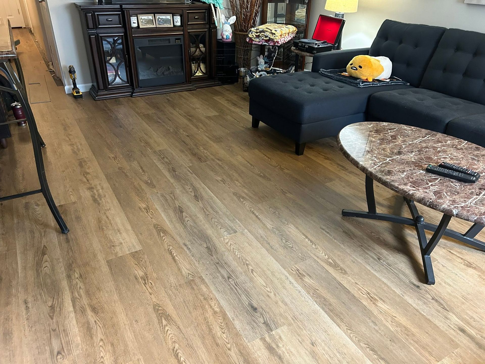 Living room with wood floors, black sectional sofa, glass coffee table, and dark TV cabinet
