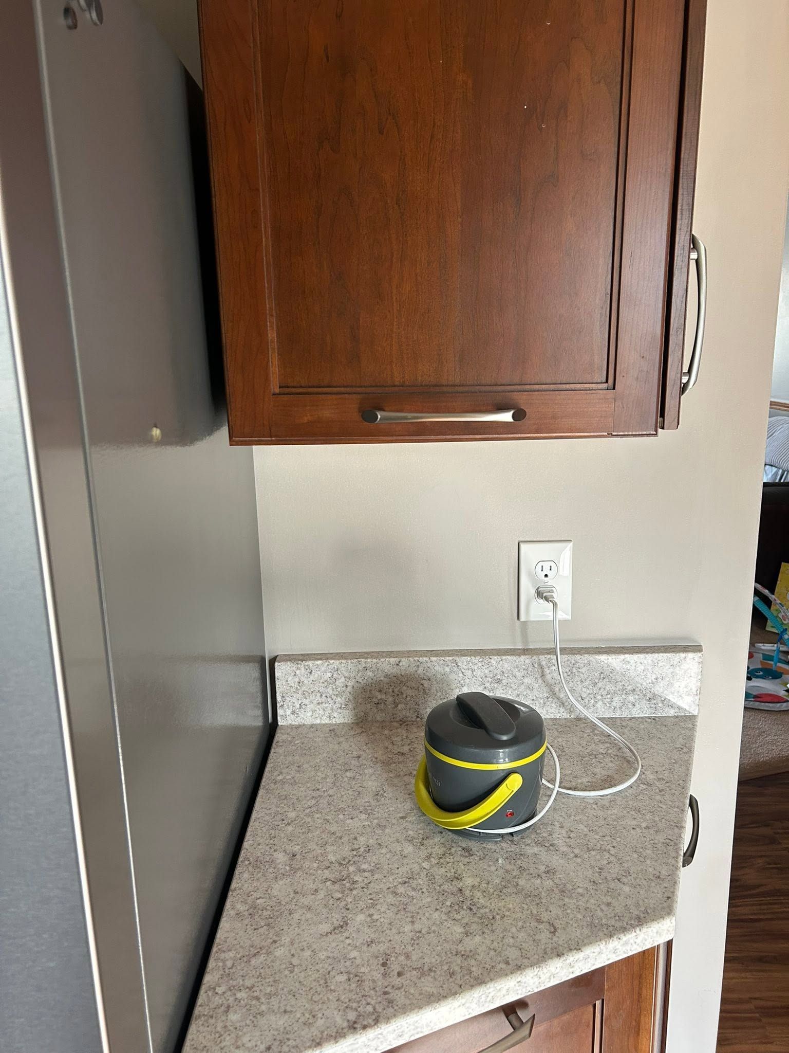 Kitchen counter with a small gray-and-yellow appliance near an outlet beneath a wooden cabinet.
