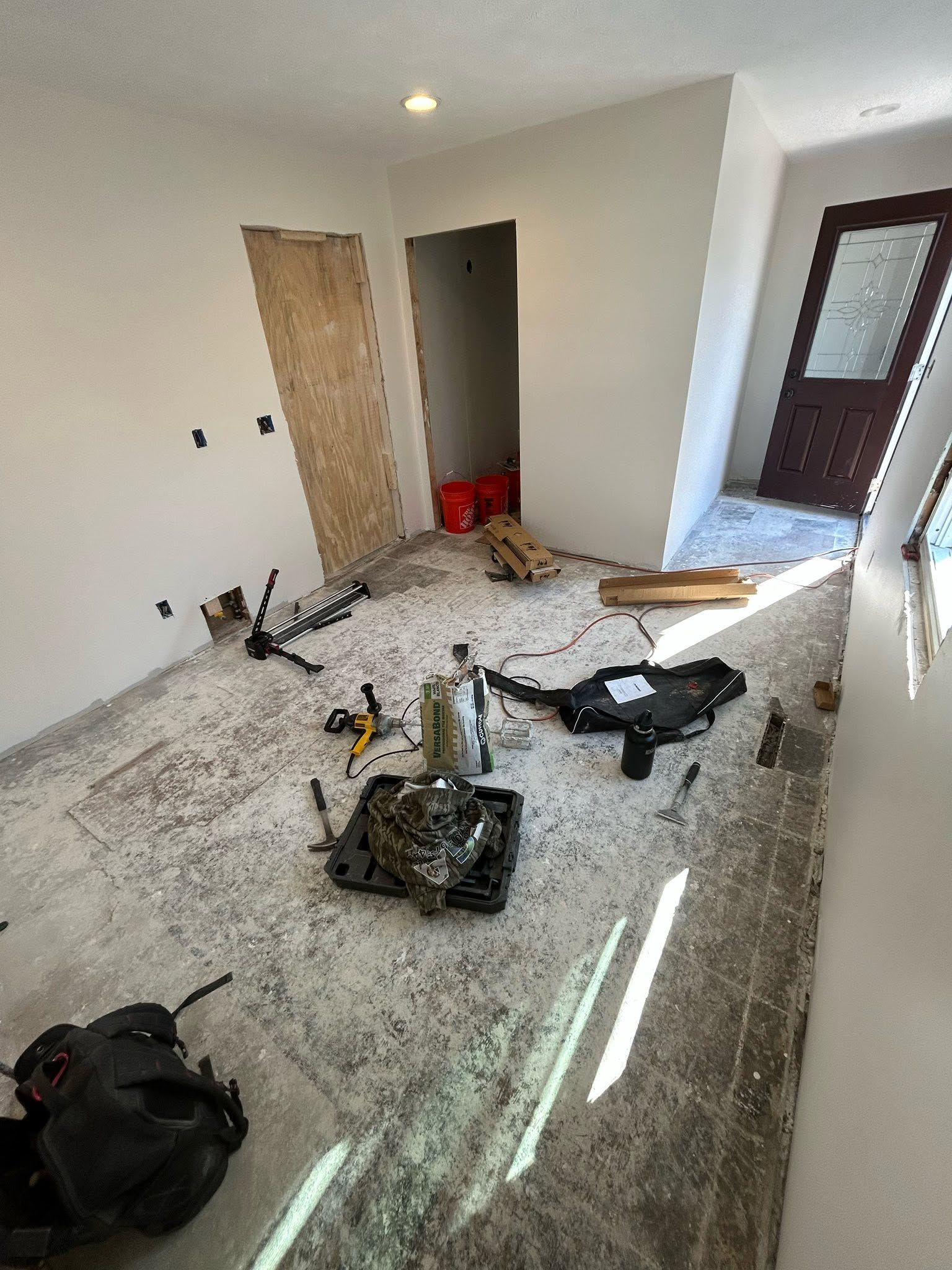 Renovation room with tools and debris on a dusty floor, boarded doorway, and sunlight through a window.
