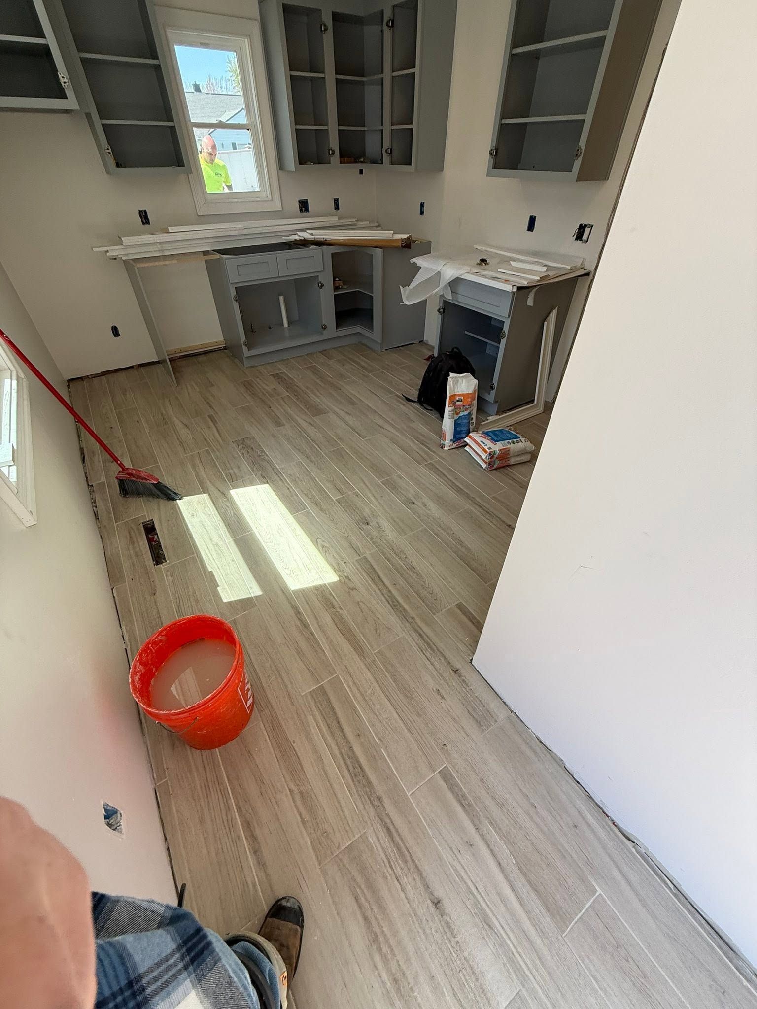 A small kitchen under renovation with white cabinets, a red bucket, and tools on the floor.